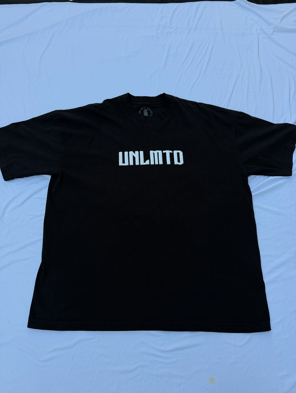 Black t shirt with white puff print letters spelling “UNLMTD”