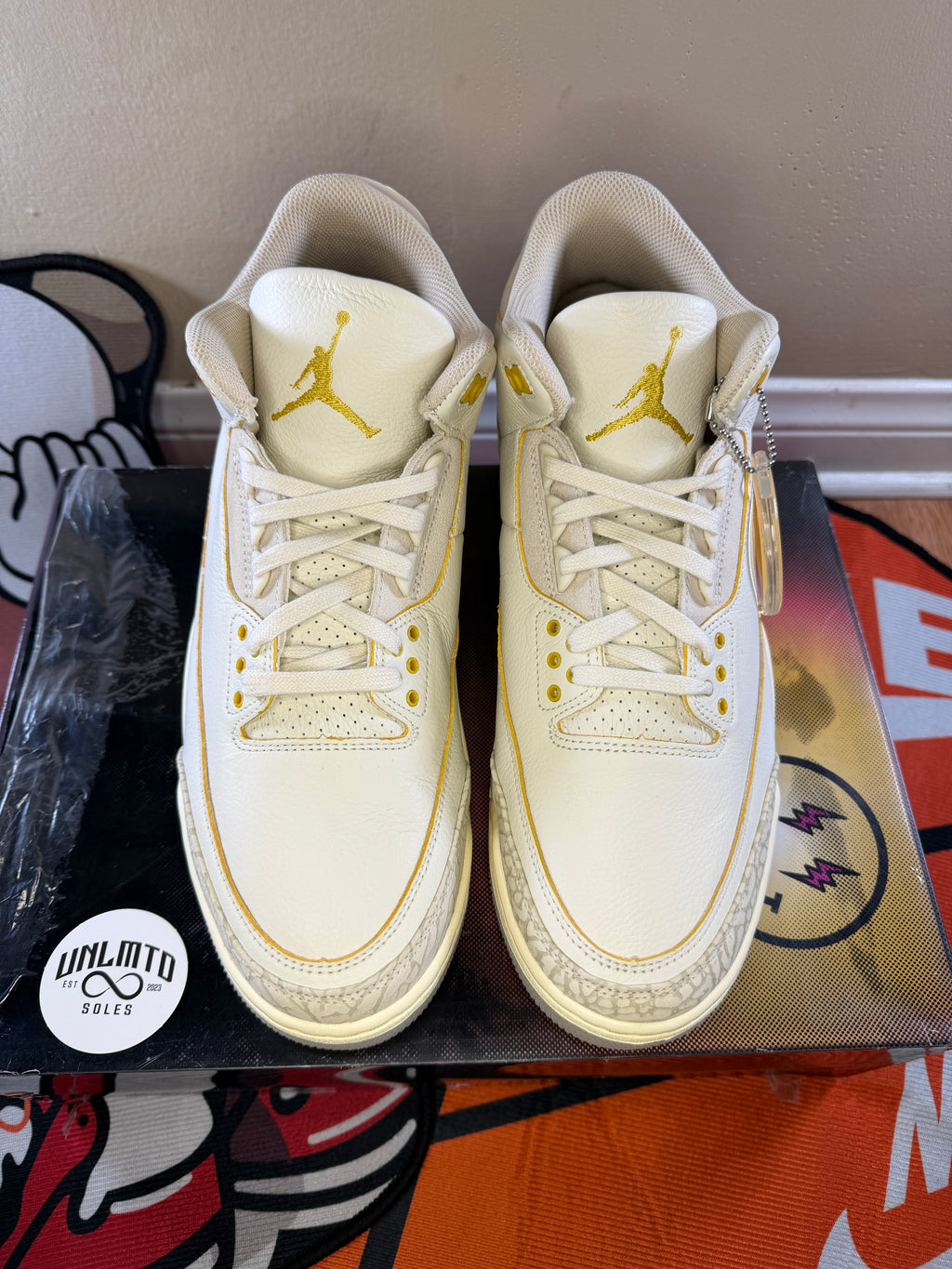 Top/Front view of shoes. Gold Jordan Logo on the tongue. Cream laces