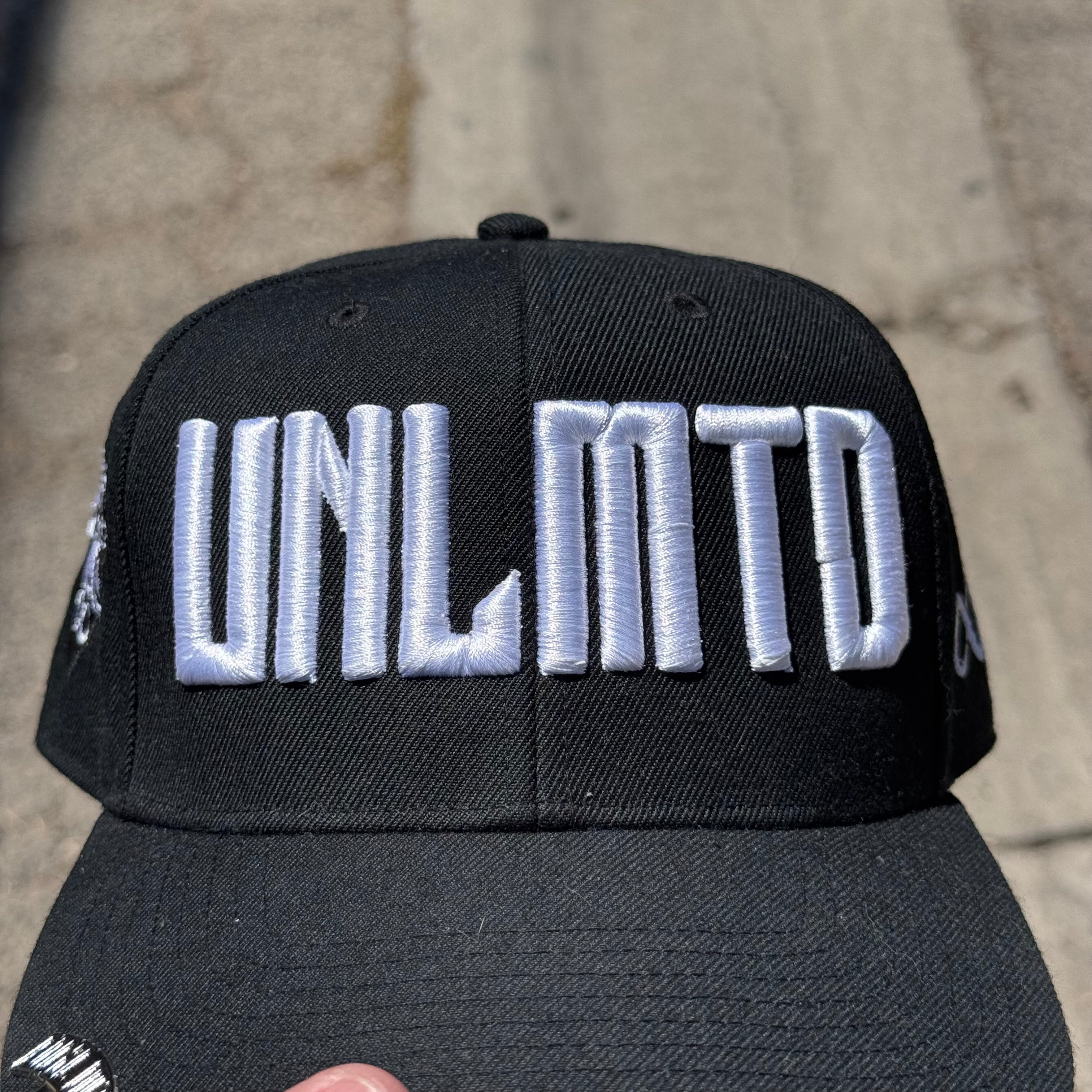Close up of white embroidered “UNLMTD” branding on black hat