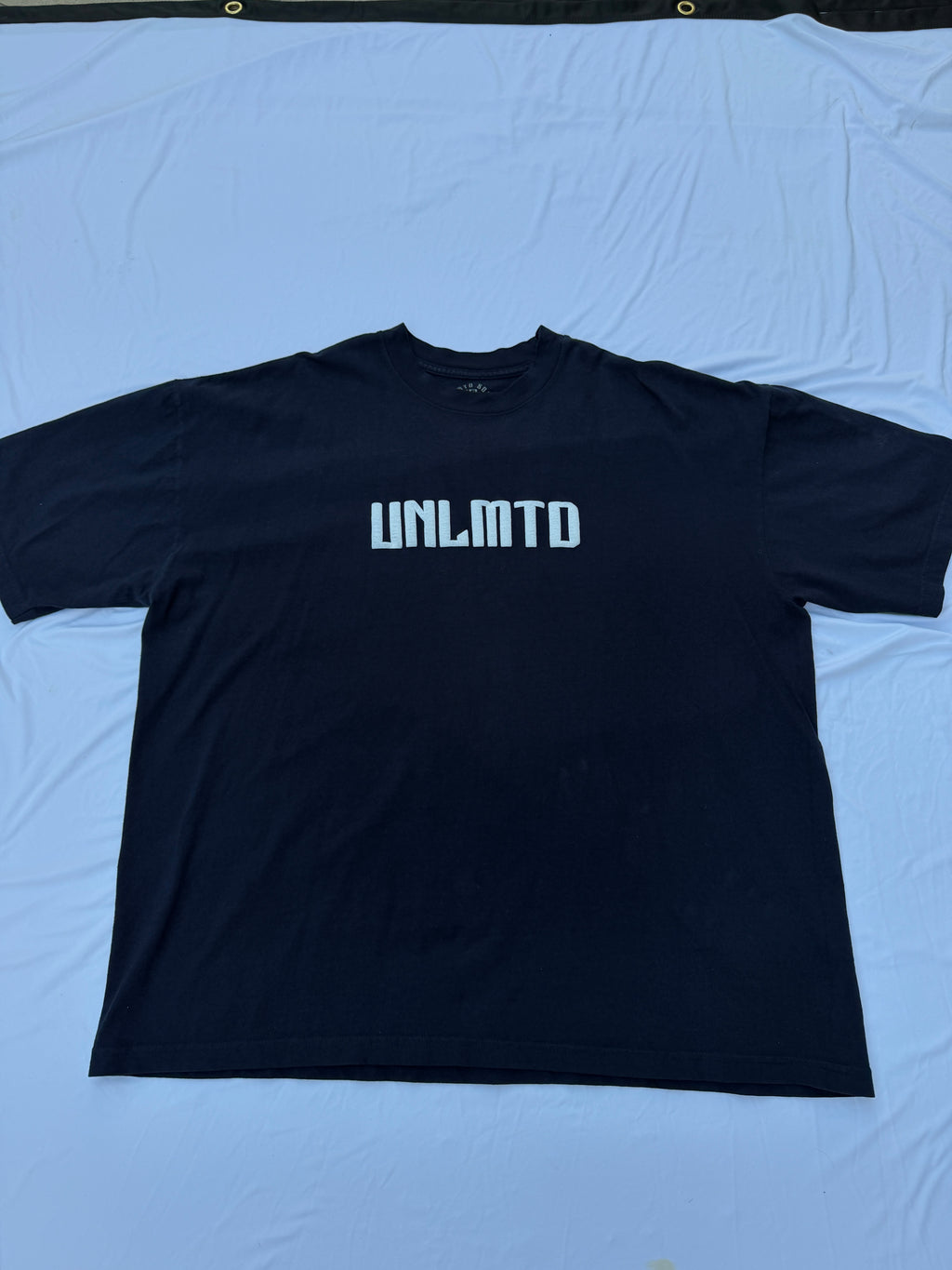 Navy blue t shirt with white puff print letters spelling “UNLMTD”