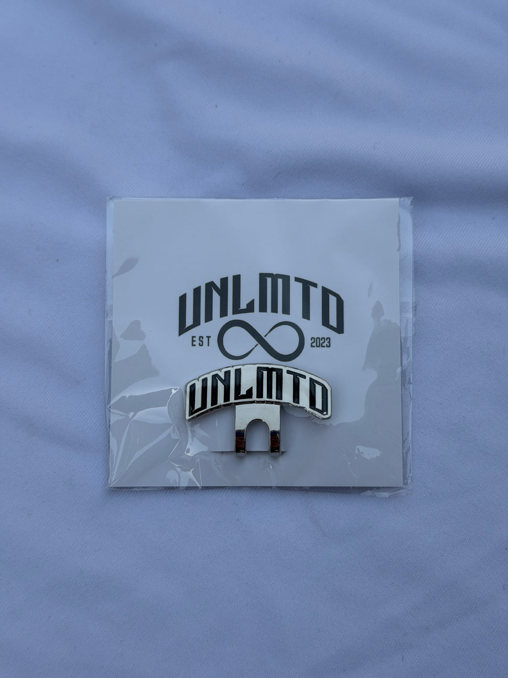 Black “UNMLTD” Clip with silver outline for brim of hat