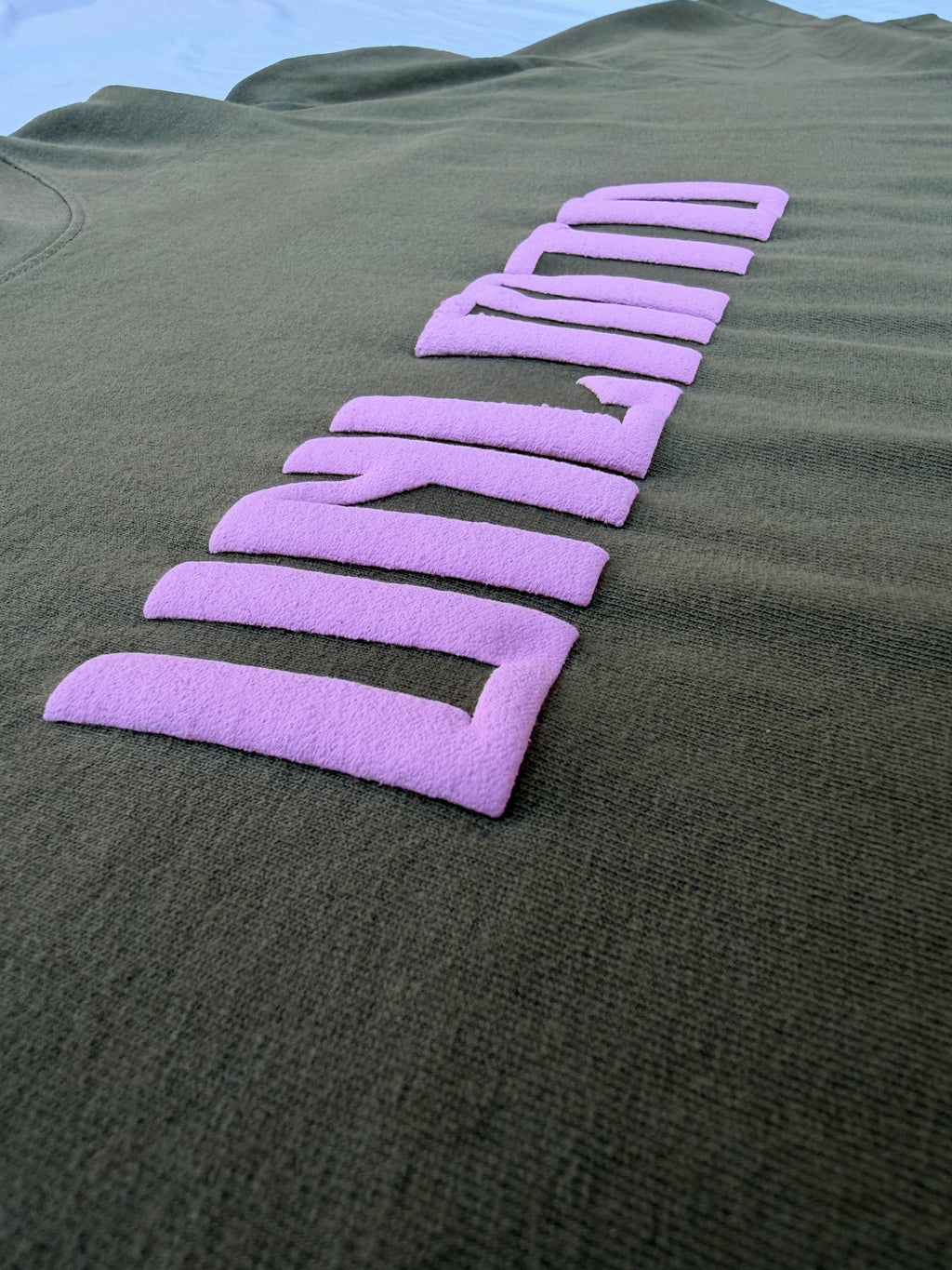 Close up of pink puff print letters on olive green shirt 