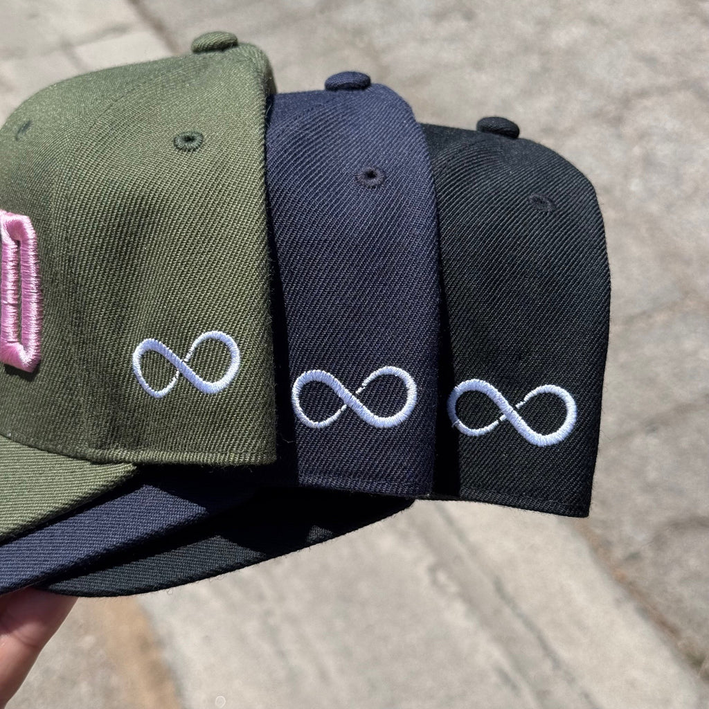 Side view of Three caps in green, navy, and black with embroidered infinity symbols